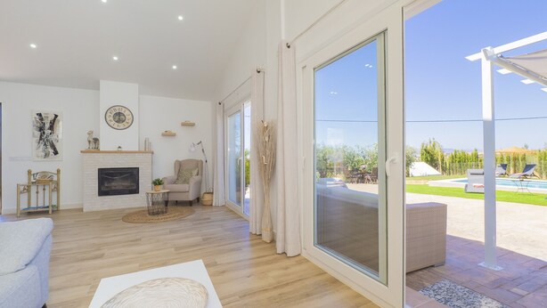 Ein geräumiges Wohnzimmer mit Kamin, eine große Schiebetür zu einem Außenbereich mit Pool und Liegestühlen.