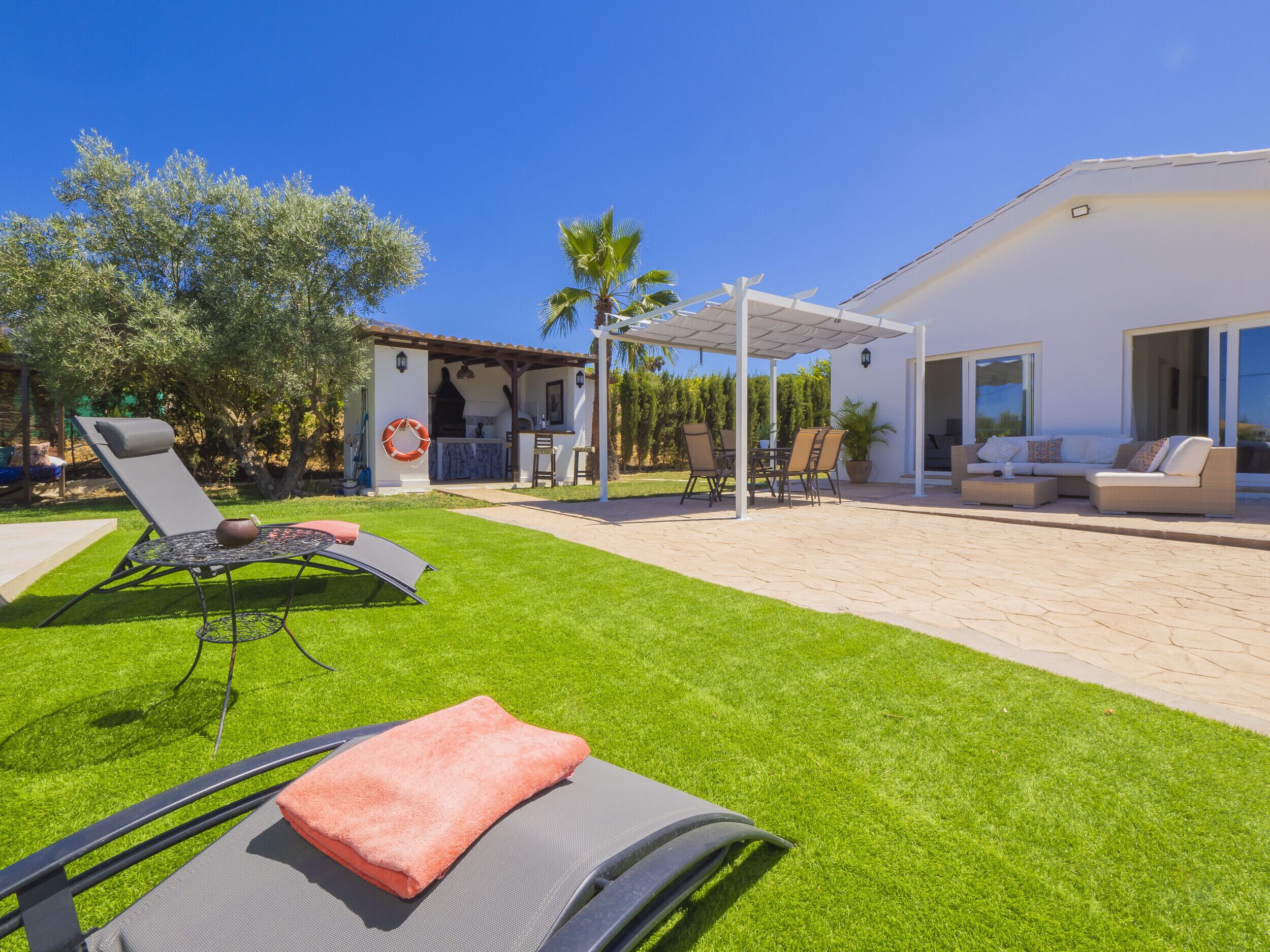Un patio con zona de estar cubierta, una parrilla y un área de descanso junto a la piscina, con toallas.