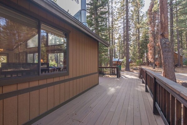 A wooden building with large windows and a deck, surrounded by tall trees.