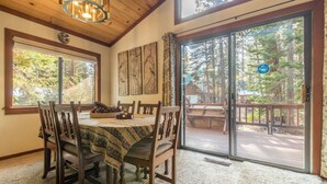 A dining area with a table set for four, wooden chairs, a chandelier, and a view of a deck with a wooden railing. - Beautiful Cabin In Tahoe Vista! (Tahoe Vista)