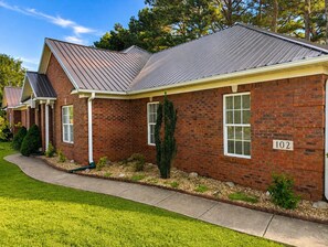 A brick building with a metal roof, numbered 102, and a well-maintained lawn.
