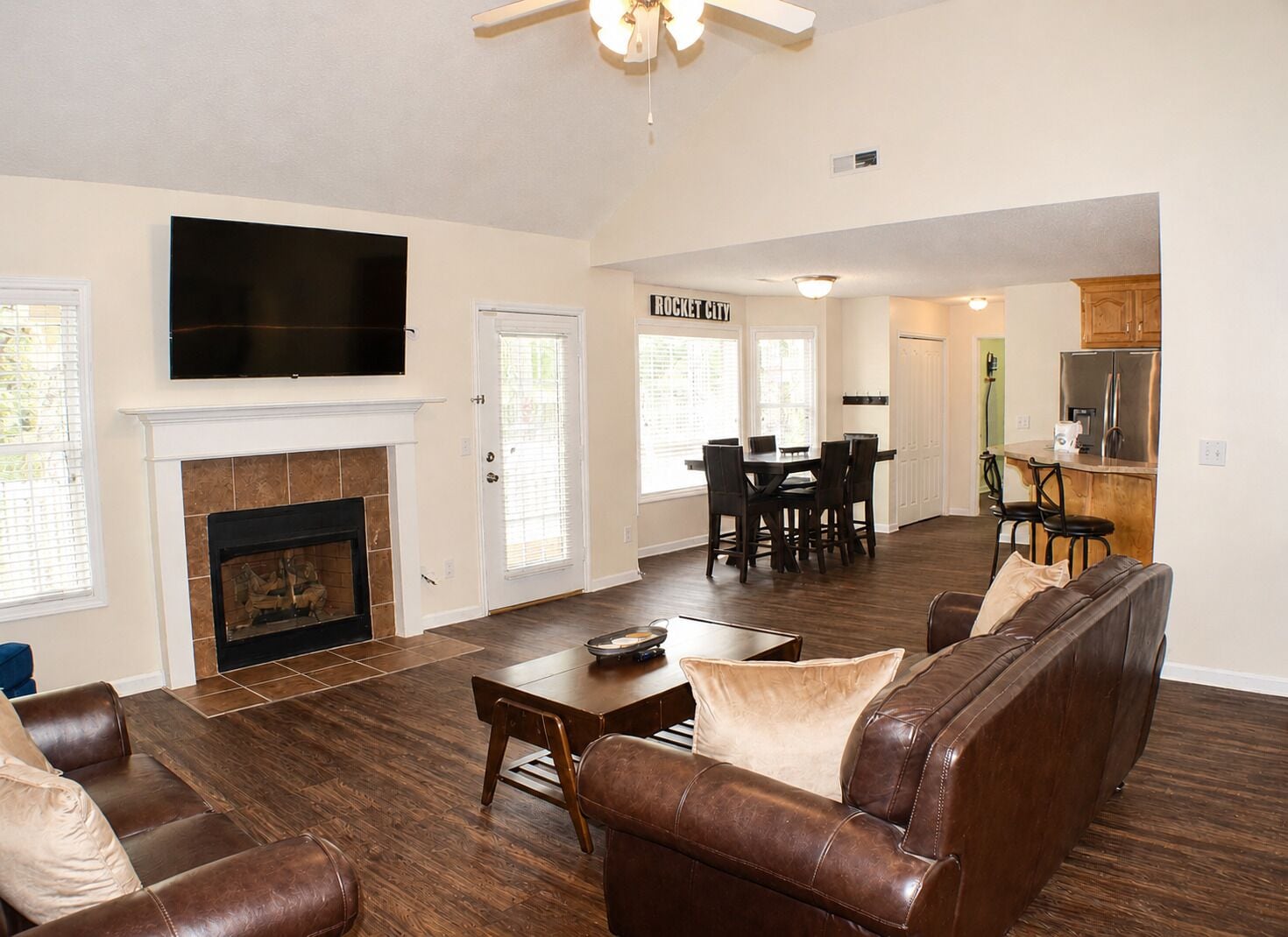 A spacious living room with a fireplace, a television mounted above it, and a dining area with a table and chairs.