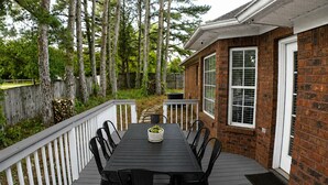 A deck with a dining table and chairs, surrounded by a wooden fence and trees. - Space Oddity: Close & Accessible! / Fiber Internet / EV Charger! (Huntsville)