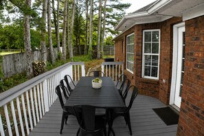 A deck with a dining table and chairs, surrounded by a wooden fence and trees.