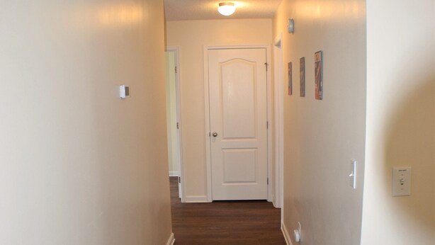 A hallway with wooden flooring, white walls, and a door at the end. - Space Oddity: Close & Accessible! / Fiber Internet / EV Charger! (Huntsville)