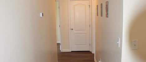 A hallway with wooden flooring, white walls, and a door at the end.