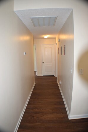 A hallway with wooden flooring, white walls, and a door at the end.