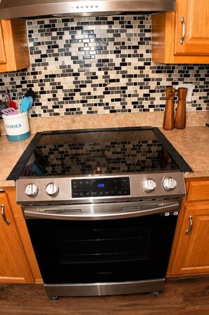 A kitchen with a stainless steel range and oven, wooden cabinets, a tiled backsplash, and a utensil holder labeled 'TOOLS'. - Space Oddity: Close & Accessible! / Fiber Internet / EV Charger! (Huntsville)