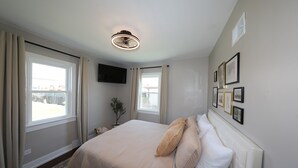Un dormitorio con una cama grande, un ventilador de techo, un televisor de pantalla plana y una ventana con cortinas.