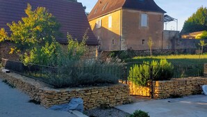 A house with a stone foundation, a red roof, and a garden with a stone wall and plants. - Piscine, Charme & Calme au Coeur du Périgord Noir (Castels et Bézenac)
