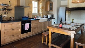 A modern kitchen with wooden cabinets, a built-in oven, and a dining area with a wooden table and benches. - Piscine, Charme & Calme au Coeur du Périgord Noir (Castels et Bézenac)