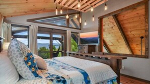 Ein Schlafzimmer mit einem großen Bett, einem Holzkopfende und Blick ins Freie durch ein großes Fenster.