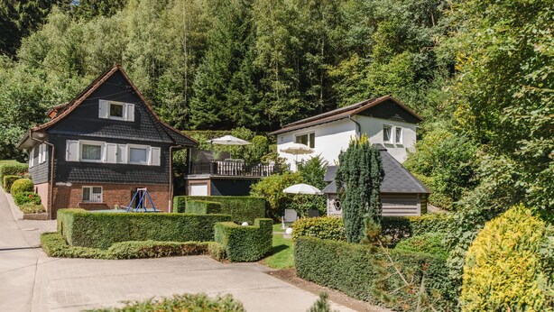 A residential area with two houses, a well-maintained garden, and a clear driveway. - Ferienhaus in Ortsrandlage mit Aussensauna und Beleuchteter Glasüberdachung (Eslohe (Sauerland))