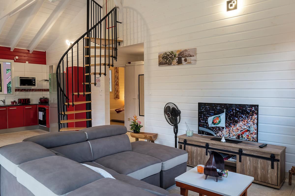 A modern living room with a grey sectional sofa, a wooden TV stand, and a staircase leading to an upper level.