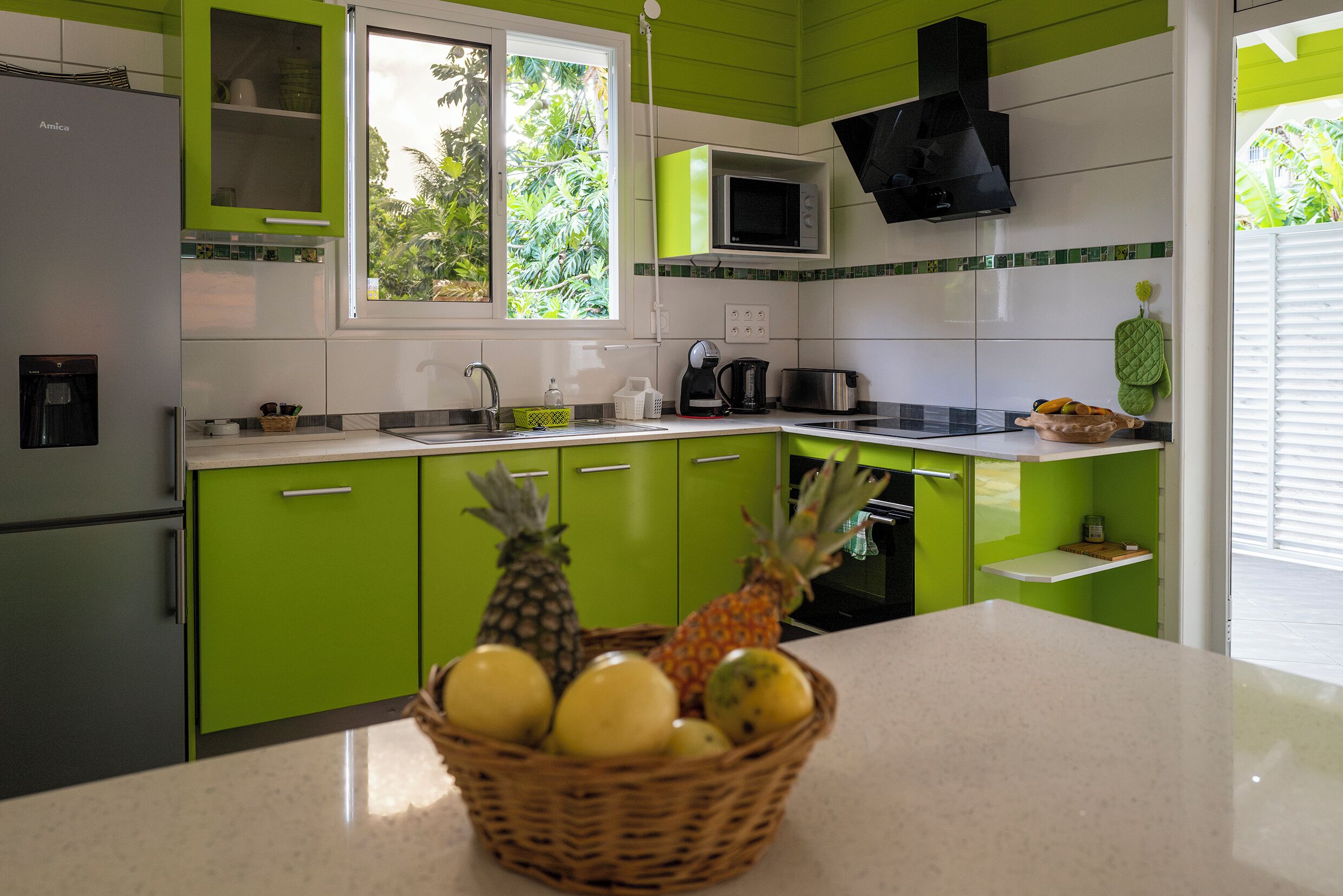 A kitchen with green cabinets, a microwave, a sink, and a fruit basket on the counter.
