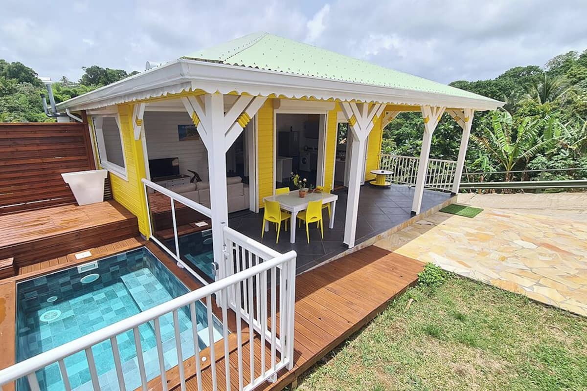 A covered outdoor area with a pool, wooden deck, and yellow chairs.