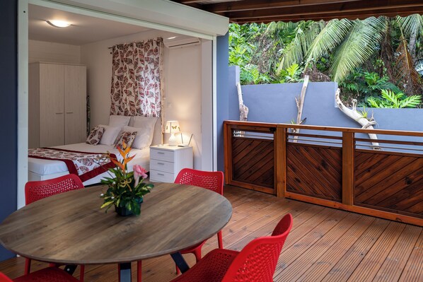 Una habitación con una cama, una mesa con sillas, una mesita de noche y un ventanal con cortinas.