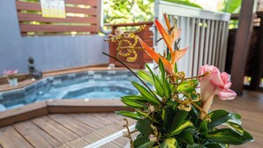Ein Whirlpool, umgeben von einer Holzterrasse, mit einem Topf mit Grünpflanzen und einer rosa Blüte im Vordergrund.