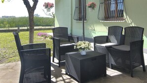 An outdoor patio with wicker furniture, a small table with a vase of flowers, and hanging flower baskets.