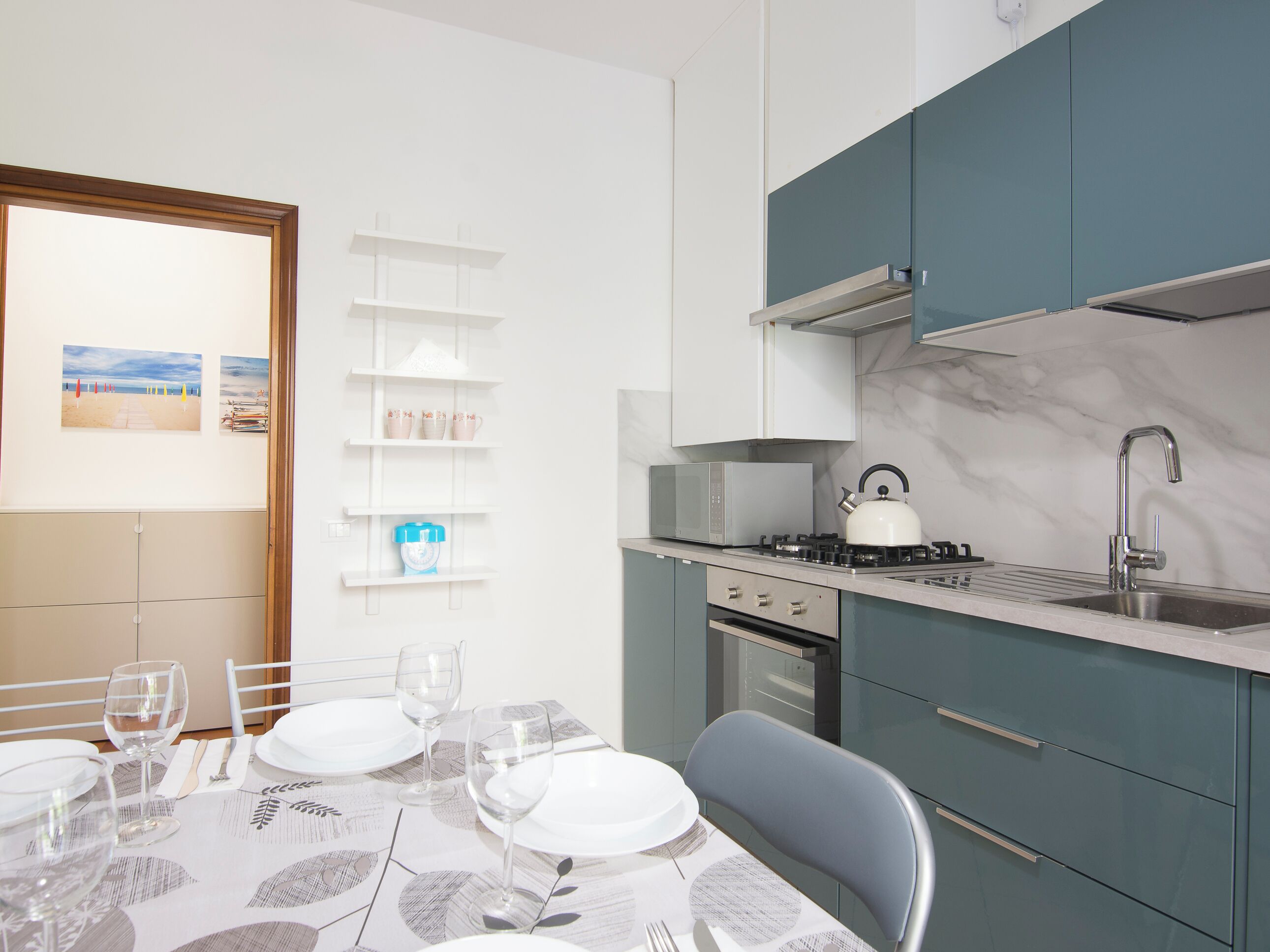 A modern kitchen with a gas stove, microwave, and stainless steel sink. There is a dining table set with plates, glasses, and cutlery.