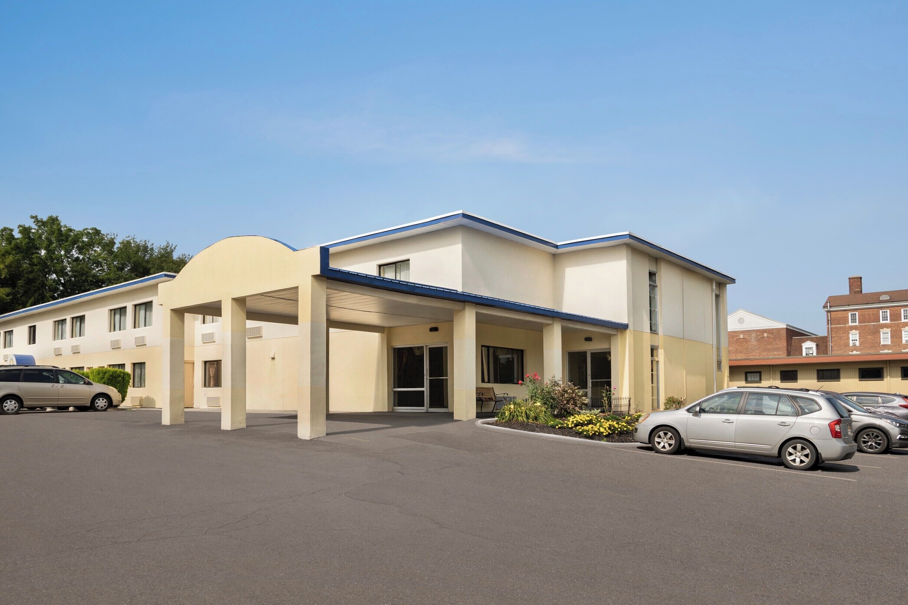 A modern hotel with a covered entrance, a parking lot, and a building with a flat roof.