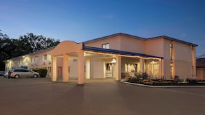 A modern hotel with a covered entrance, multiple windows, and a parking lot with cars. - The Cayuga Inn at the Finger Lakes (Auburn)
