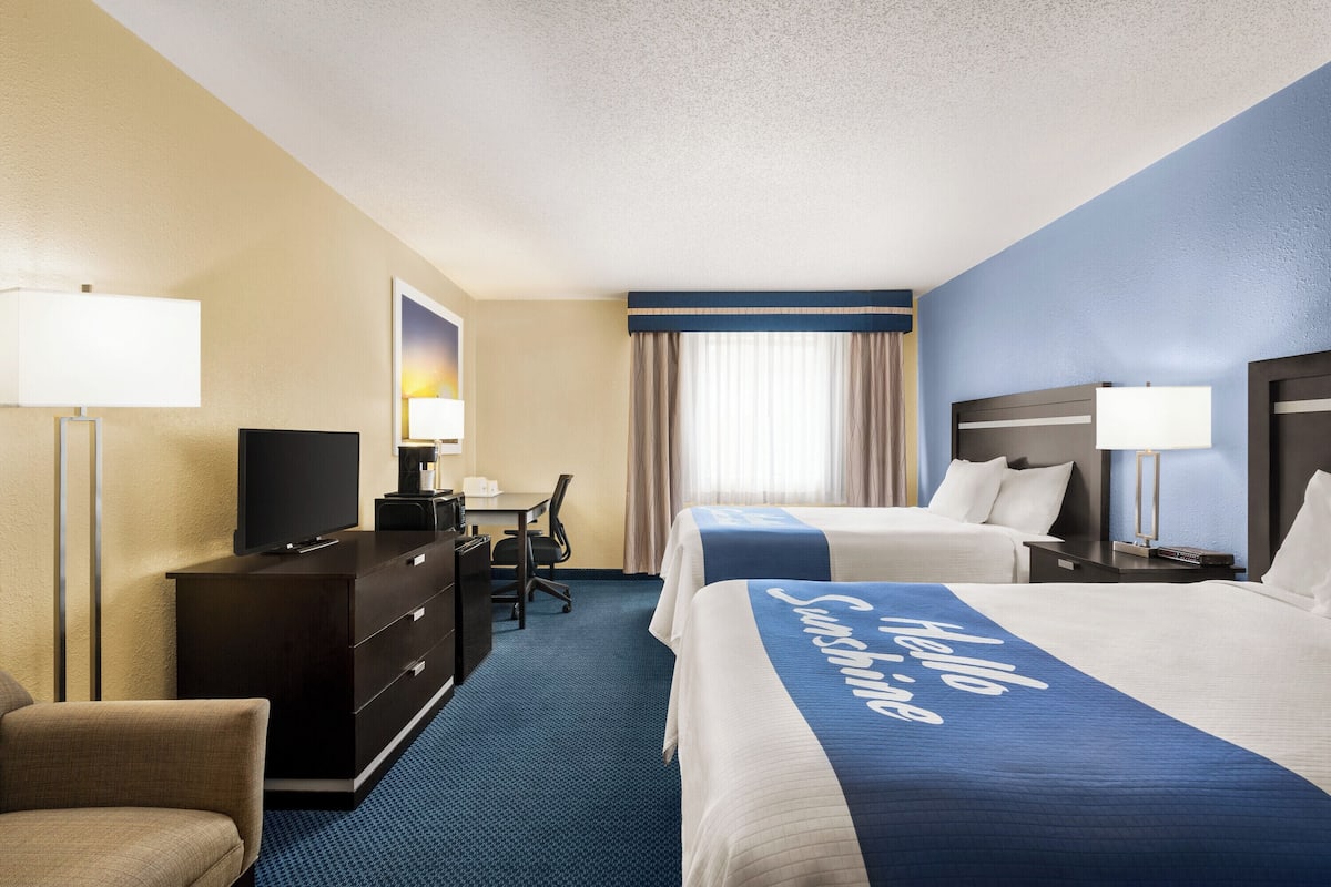 A hotel room with two beds, a desk, a chair, a TV, and a dresser.