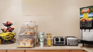 A breakfast bar with a fruit bowl, bread display, yogurt containers, and two toasters. - The Cayuga Inn at the Finger Lakes (Auburn)
