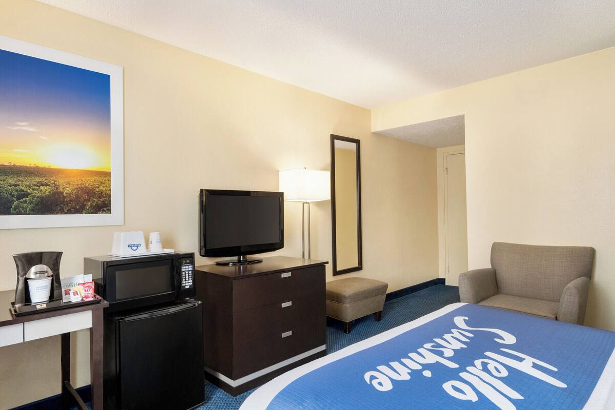 A hotel room with a bed, a TV, a microwave, a desk, a chair, and a nightstand.