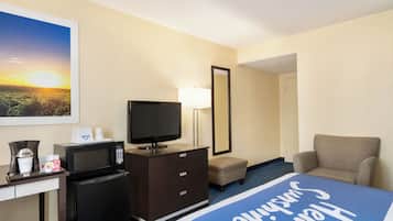 A hotel room with a bed, a TV, a microwave, a desk, a chair, and a nightstand.