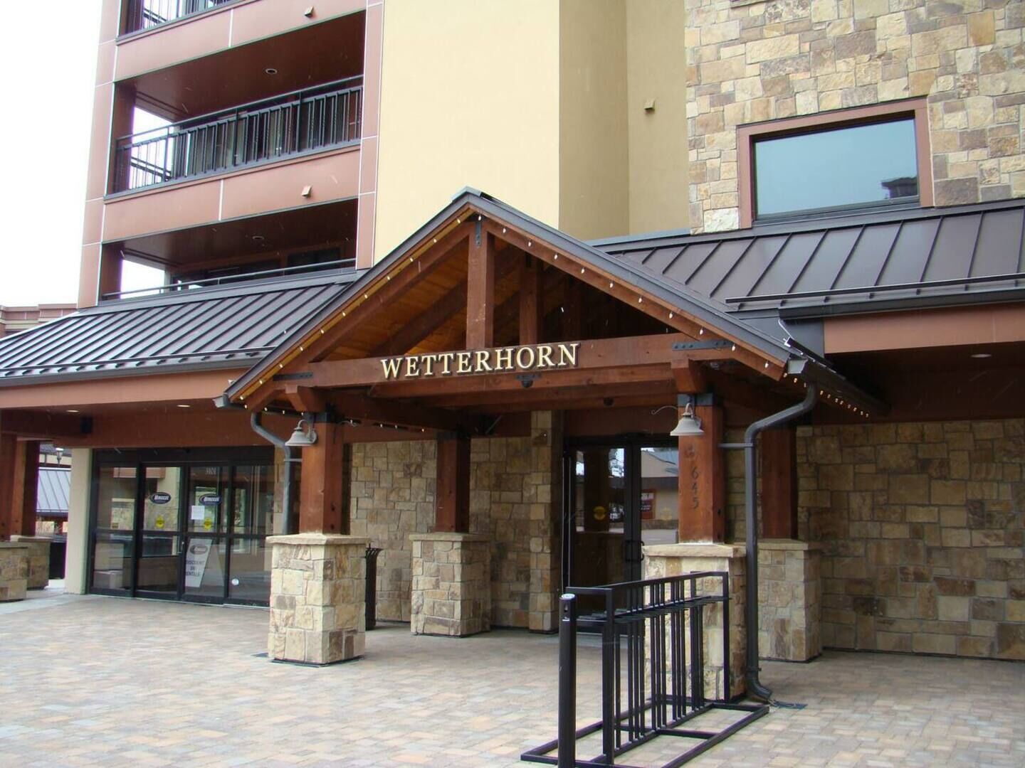 L’entrée d’un hôtel, avec une façade en pierre, un auvent en bois et une rambarde en métal.