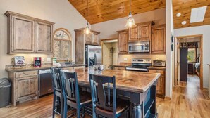 A spacious kitchen with wooden cabinets, a large island with chairs, stainless steel appliances, and a high wooden ceiling. - Lovely Cabin on Appalachian Ski Mountain (Blowing Rock)