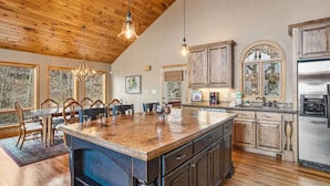 A spacious kitchen with wooden cabinets, a large island, and a dining area with a chandelier. - Lovely Cabin on Appalachian Ski Mountain (Blowing Rock)