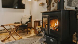 Ein gemütliches Wohnzimmer mit Kaminofen, bequemen Sessel und flachbildfernseher an der Wand.