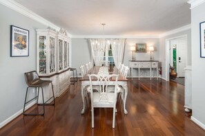 A dining room with a long table, white chairs, a white cabinet, and a chandelier.