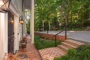 Ein Backsteinweg führt zu einem Haus mit einer dunklen Tür, einem Blumentopf und einer Holzpergola.