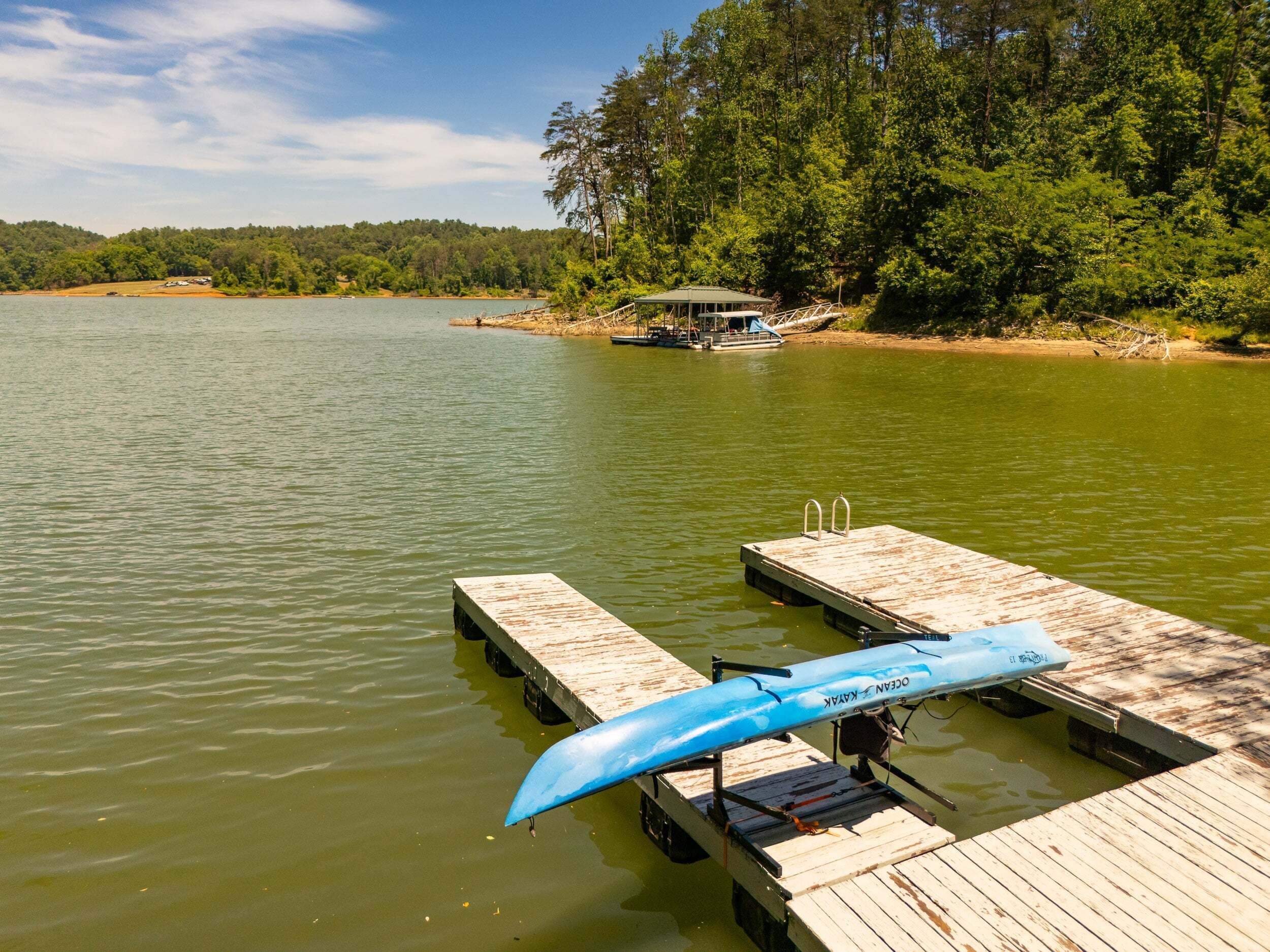 A wooden dock extending into a calm lake with a boat and a canopy structure on the opposite shore.