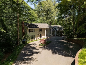 A two-story house with a driveway leading to the entrance, surrounded by dense trees.