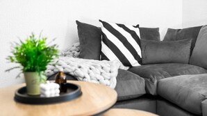 A modern living room with a gray sectional sofa, a black and white striped pillow, a green plant, and a wooden coffee table.