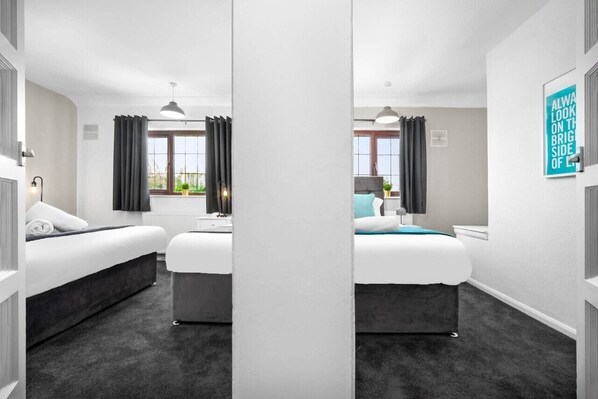 Habitación de hotel moderna con dos camas, un ventanal con cortinas y vistas a zonas verdes, además de una frase motivadora en la pared.