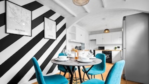 A modern kitchen with white cabinets, a built-in oven, and a dining area with a round table and blue chairs.