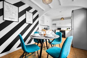 Eine moderne Küche mit weißen Schränken, einem eingebauten Backofen und einem Essbereich mit einem runden Tisch und blauen Stühlen.