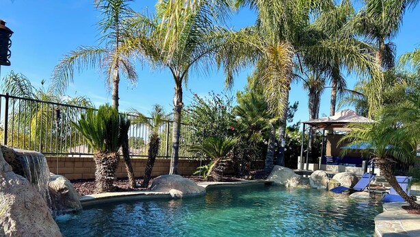 A clear pool with a waterfall feature, surrounded by palm trees and rocks. - 5-10 mins to Temecula WineCountry; resort-like pool spa w/ amazing sunset views! (Winchester)