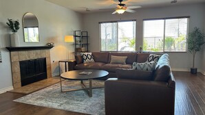 A living room with a fireplace, a ceiling fan, and large windows. - 5-10 mins to Temecula WineCountry; resort-like pool spa w/ amazing sunset views! (Winchester)