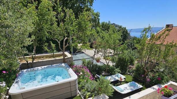 A hot tub surrounded by lush greenery and potted plants, with a view of the sea in the background. - Holiday Home Sunrise - Three Bedroom Holiday Home (Omis)