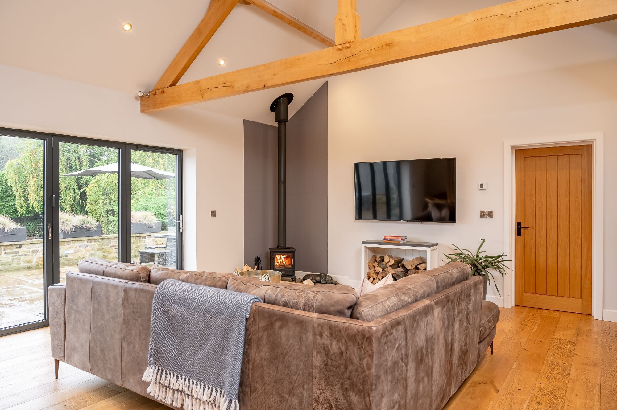 A modern living room with a large sofa, a fireplace, a TV mounted on the wall, and a wooden door.