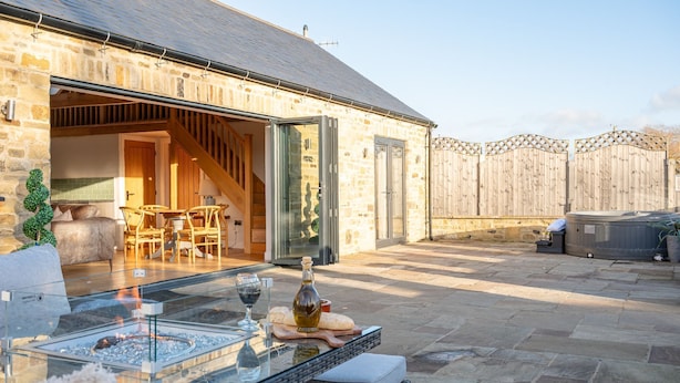 A stone building with a glass patio, outdoor seating, and a hot tub.