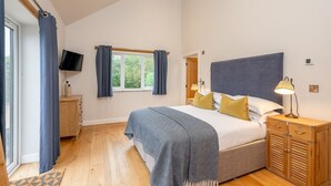 A bedroom with a bed, a TV, a window with curtains, a bedside lamp, and a wooden cabinet.