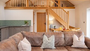 A cozy living area with a brown leather sofa, wooden staircase, and a dining table with breakfast items.