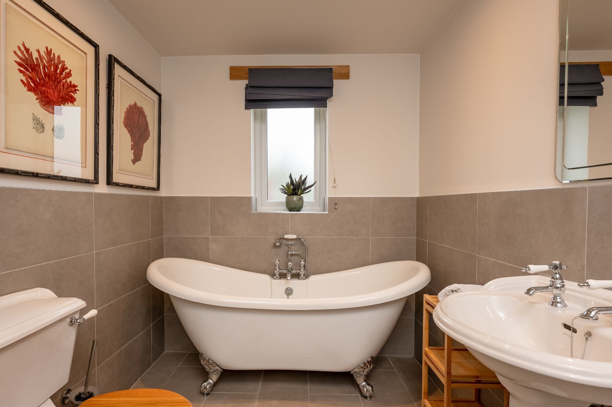 Un baño con una bañera independiente, un lavamanos y una ventana con una planta.